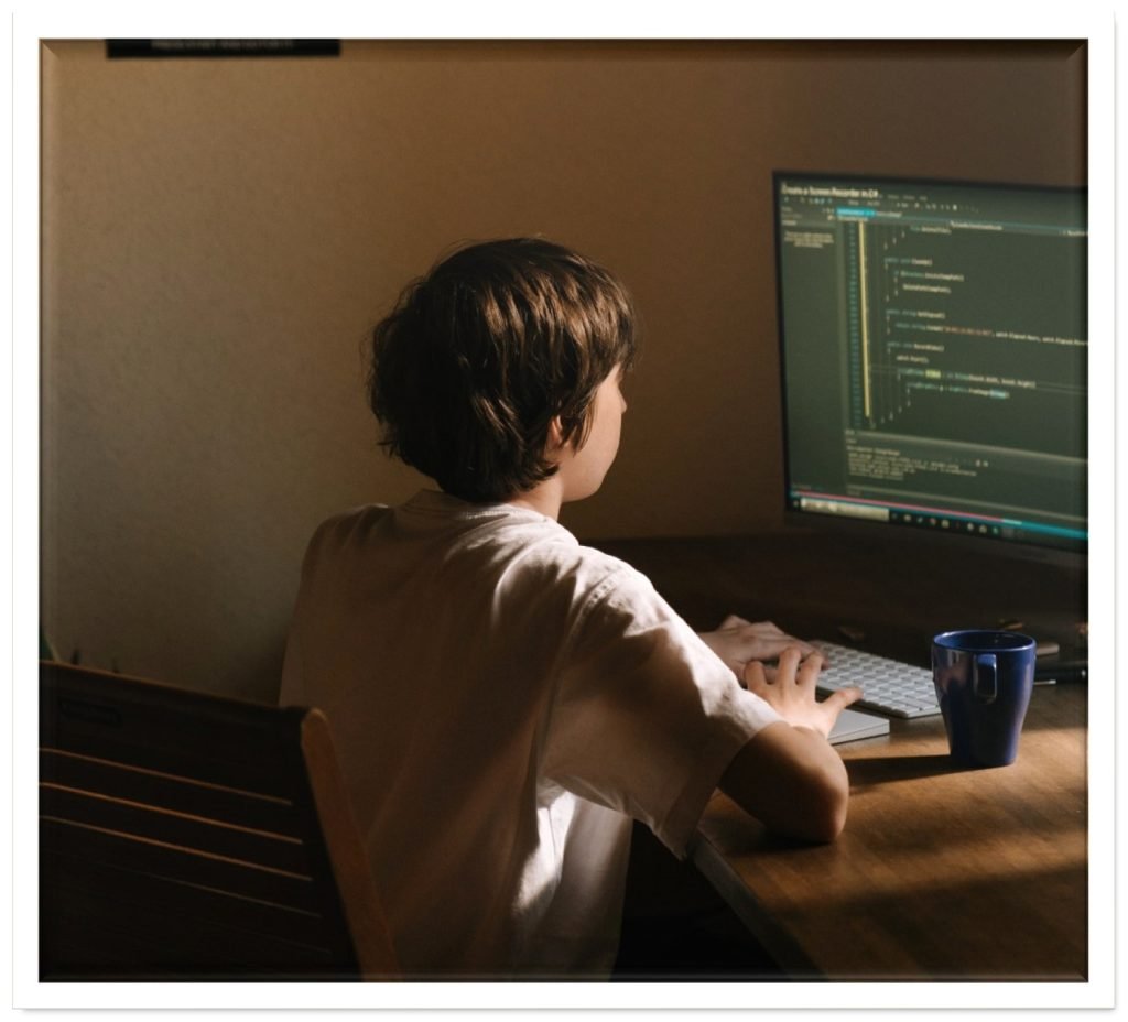 Pre-teen boy sat at a desk typing code into a computer